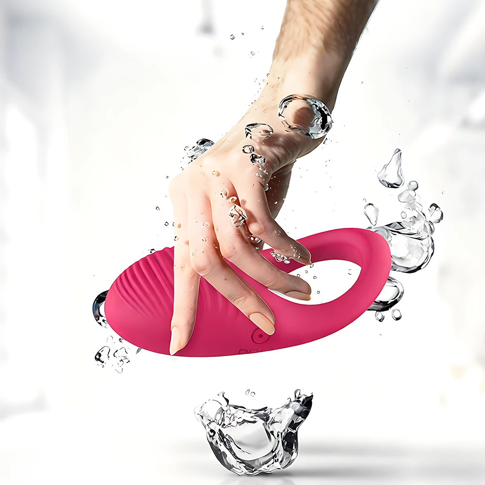 Serica Penis Ring in pink luxuriously soft silicone; waterproof textured loop handle held in hand with water splashes.