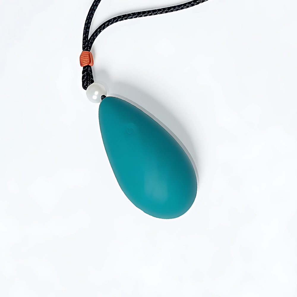 Back-angle product image of the NOIR Clitoral Vibrator in deep teal, featuring a sleek teardrop silhouette with a soft matte finish and a subtle power icon embossed near the top. The device is attached to a black cord with a white bead and brown accent, emphasizing its wearable, discreet design. The composition showcases NOIR’s luxuriously soft silicone surface and ergonomic contours, reinforcing its identity as a premium, sensual wellness product designed for comfort and control.