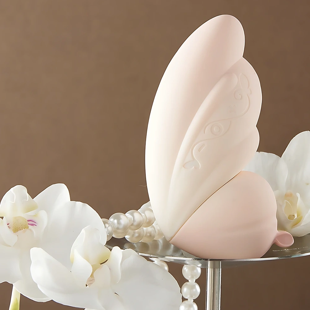 TAOF Liberty Blush upright butterfly massager on glass stand with white orchids and pearls, showing engraved silicone details.