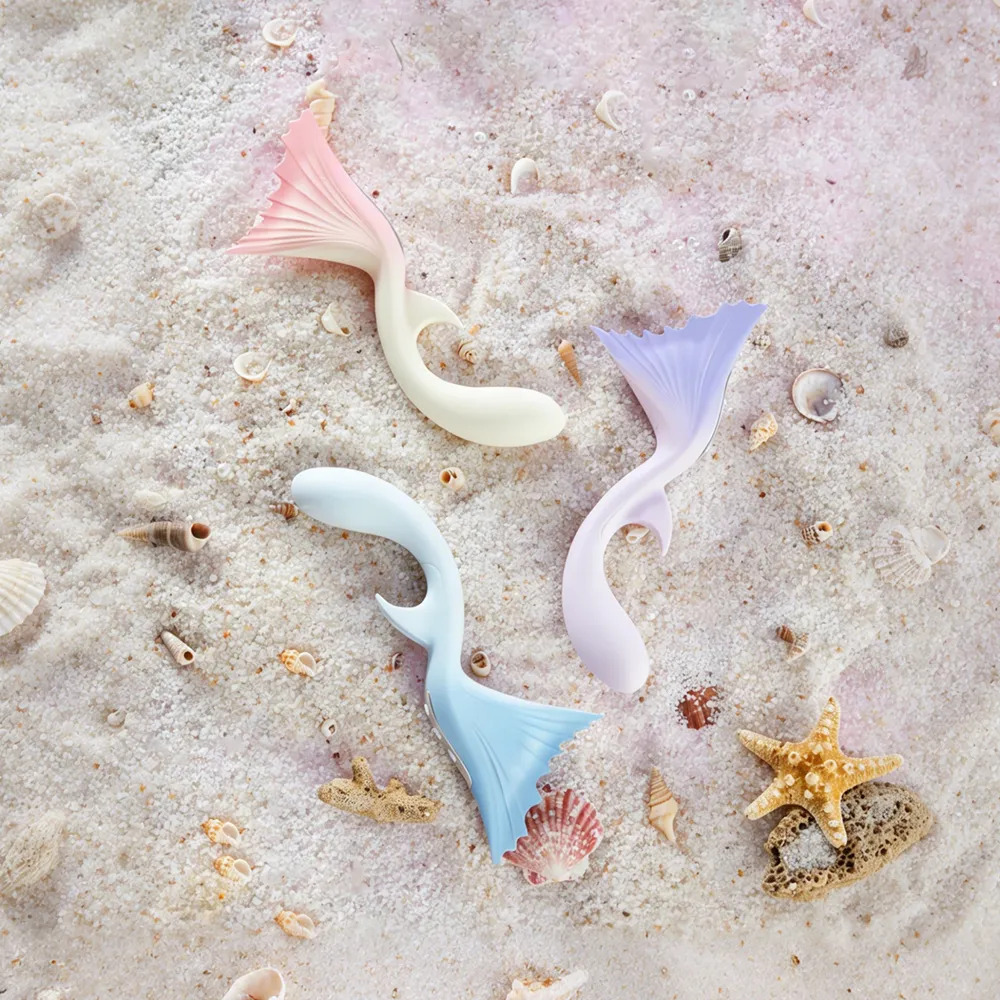Three delicate TAOF Vivare massagers in soft pastel shades resting gracefully on a sandy beach with seashells, showcasing the collection's versatile color options for every mood.